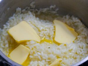 Butter und Parmesan zum Risotto geben
