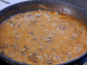 Fertige Sauce für Kritharaki-Auflauf mit Kritharaki Nudeln vermengen