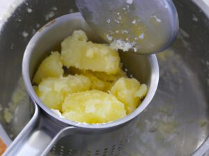 Gar gekochte Kartoffeln in eine Kartoffelpresse geben für Püree