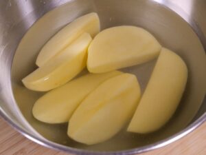 Geschnittene Kartoffeln in Schüssel mit kaltem Wasser geben
