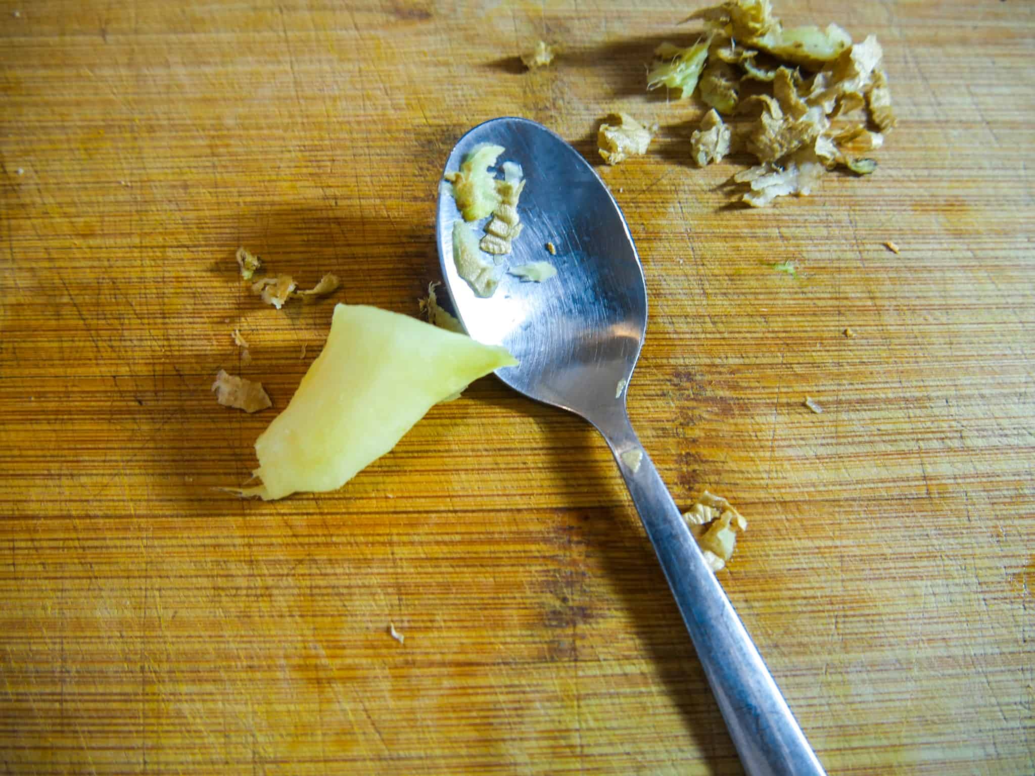 Ingwer für die leichte Kürbissuppe mit einem Löffel schälen