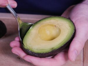 Mit Löffel Fruchtfleisch von Avocado lösen für Guacamole