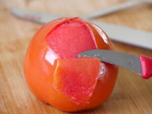 Schale der Tomate für Zucchinifüllung mit einem kleinen Messer entfernen