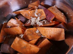 Süßkartoffelwedges mit Öl Knoblauch und Gewürzen mischen