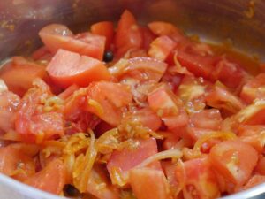 Tomaten zu den Zwiebeln geben und aufkochen lassen