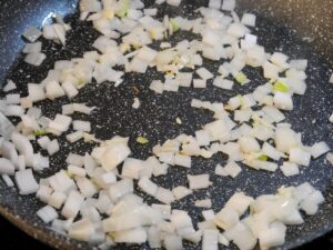 Zwiebeln und Knoblauch in Pfanne für Kritharaki-Auflauf anschwitzen